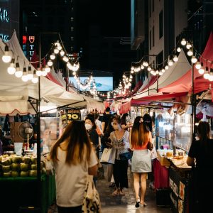 Bustling night market scene with shoppers exploring colorful stalls and string lights.