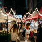 Bustling night market scene with shoppers exploring colorful stalls and string lights.